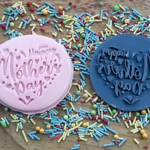 Puede incluir: Dos sellos de silicona, uno rosa y otro azul, con el texto "Happy Mother's Day" en forma de coraz&oacute;n. Los sellos est&aacute;n rodeados de espolvoreados coloridos.
