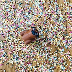 Op de afbeelding: Een bruin speelgoedpug met goggle-ogen is omringd door kleurrijke sprinkels op een houten oppervlak.