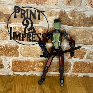 May include: A multi-coloured articulated action figure holding a black sword. The figure has a green head and chest, with red, blue, and brown accents. The figure is posed in front of a brick wall with the text "PRINT 2 IMPRESS" in a black circle.