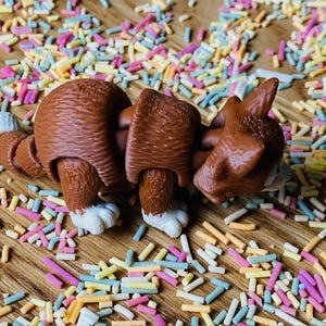May include: A brown and white segmented toy dog with a playful expression. The dog is lying on a surface covered in colorful sprinkles.