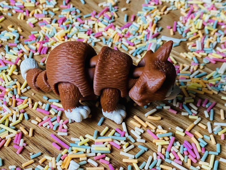 May include: A brown and white segmented toy dog with a playful expression. The dog is lying on a surface covered in colorful sprinkles.