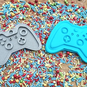 以下が含まれることがあります： ビデオゲームコントローラーのプラスチック製の型が2つあります。1つはグレーで、もう1つはブルーです。型はカラフルなスプリンクルで覆われた表面にあります。