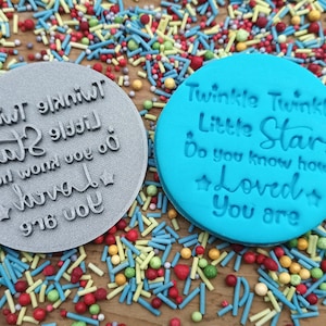 May include: Two round silicone molds for baking. The blue mold says "Twinkle Twinkle Little Star Do you know how Loved You are." The gray mold says "Twinkle Twinkle Little Star Do you know how Loved You are." Both molds are surrounded by colorful sprinkles.
