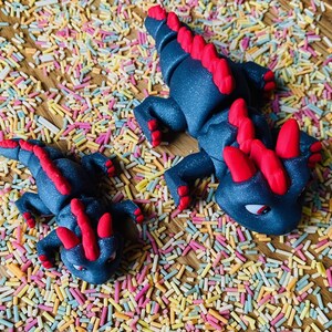 May include: Two black and red dragon figurines on a background of colorful sprinkles. The larger dragon is about 6 inches long and the smaller dragon is about 3 inches long.