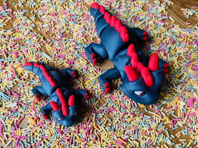 May include: Two black and red dragon figurines on a background of colorful sprinkles. The larger dragon is about 6 inches long and the smaller dragon is about 3 inches long.