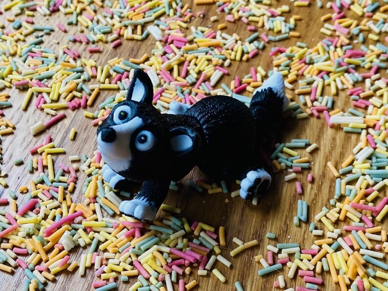 May include: A black and white toy dog figurine with a playful expression, lying on a surface covered in colorful sprinkles.