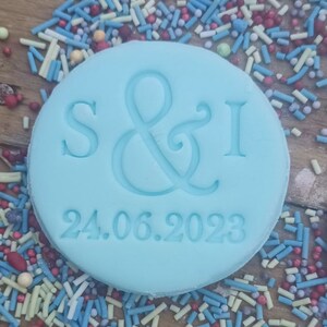 May include: A light blue round cookie with the letters "S&I" and the date "24.06.2023" embossed on it. The cookie is surrounded by colorful sprinkles.
