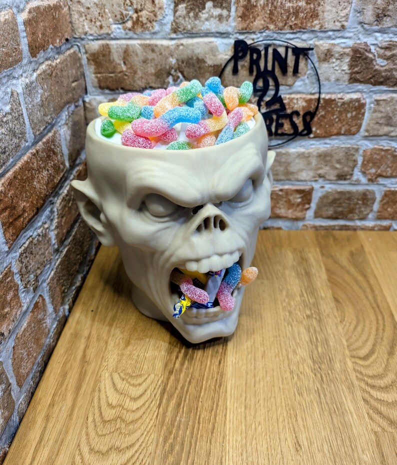 May include: A beige skull-shaped container filled with colorful gummy candies. The container has a wide open mouth with candies spilling out. The candies are in various colors, including pink, yellow, blue, and green.