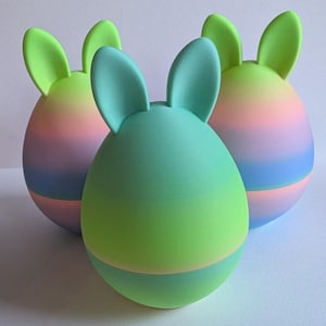 May include: Three pastel ombre Easter eggs with bunny ears. The eggs are green, pink, and blue.