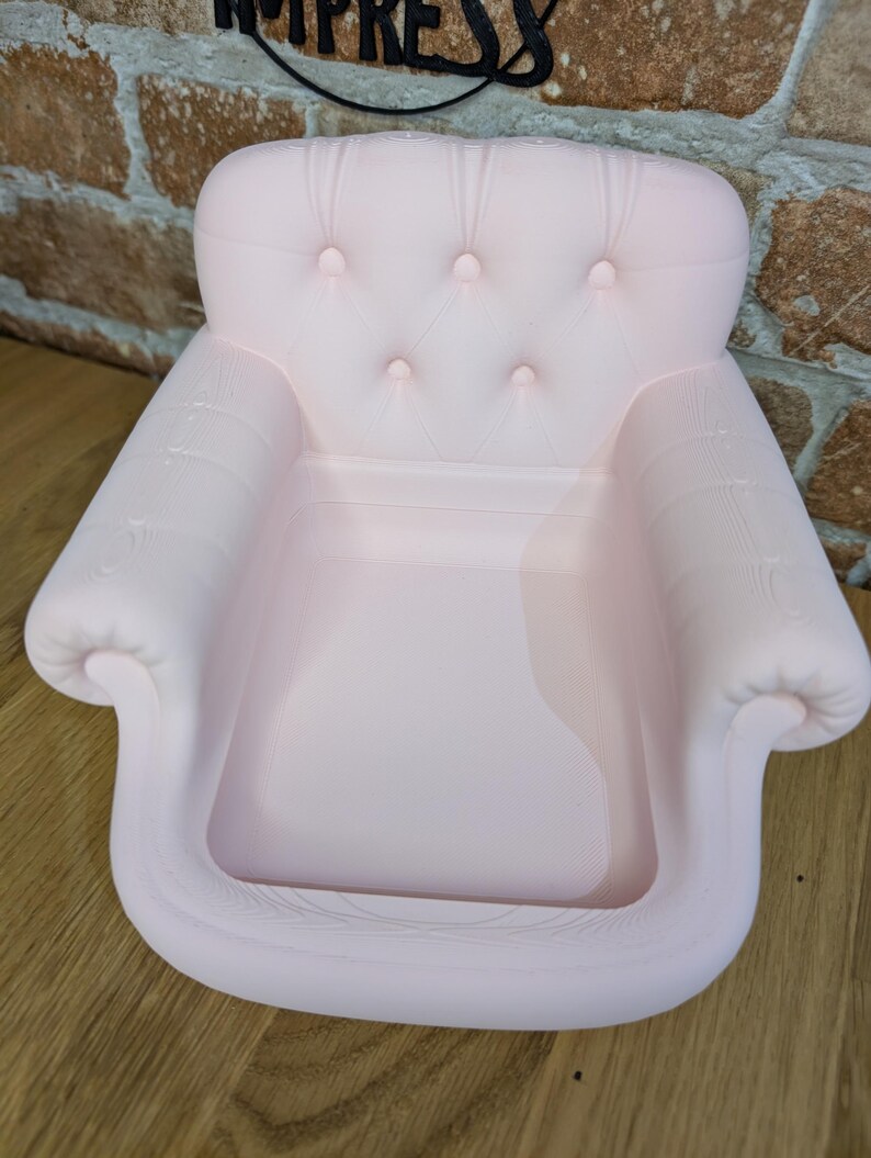 May include: A light pink miniature armchair with a tufted back and armrests. The small chair has a classic design with button detailing and a recessed seat. The chair is made of a solid material and is designed to be a decorative item.