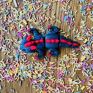 May include: A black and red play dough dragon on a wooden surface covered in colorful sprinkles.