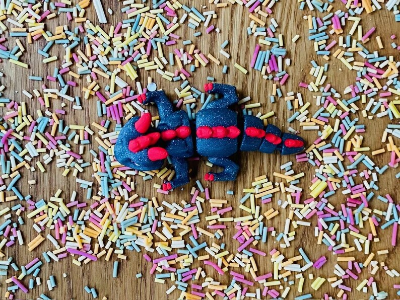 May include: A black and red play dough dragon on a wooden surface covered in colorful sprinkles.