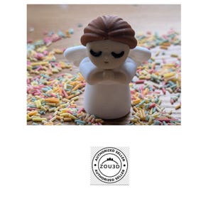 May include: A white angel figurine with brown hair and closed eyes, standing on a wooden surface covered in colorful sprinkles.