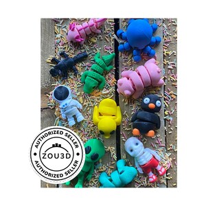 May include: A collection of 10 colorful 3D printed figurines, including a pink pig, a yellow chick, a blue octopus, a green alien, a black and white penguin, a white astronaut, a green crocodile, a black scorpion, a pink centipede, and a skeleton with red shorts. The figurines are on a wooden surface with colorful sprinkles.