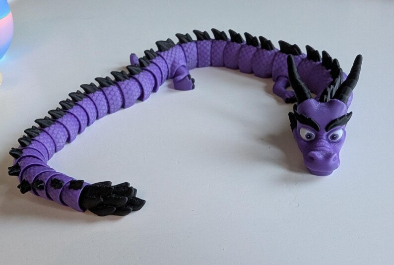 K&ouml;nnte beinhalten: Ein lila-schwarzes, segmentiertes Drachenspielzeug mit einem detaillierten Kopf und gro&szlig;en Augen. Der Drache ist in einer geschwungenen Form aufgestellt.