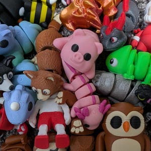 May include: A collection of colorful, articulated animal figurines. The assortment includes a pink pig, green chameleon, brown owl, and a Santa Claus figure. Other animals include a monkey, dog, and alien.