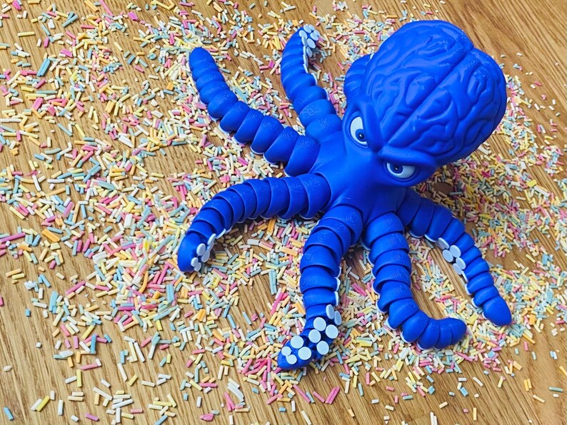 May include: A bright blue octopus toy with a detailed brain-like head and expressive eyes. The octopus is surrounded by colorful sprinkles on a wooden surface, creating a playful and whimsical scene.