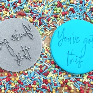 以下が含まれることがあります： 「Top of the zitt」の文字が入ったグレーのクッキー型と、「You've got this」の文字が入った青色のクッキー型。カラフルなスプリンクルで囲まれています。
