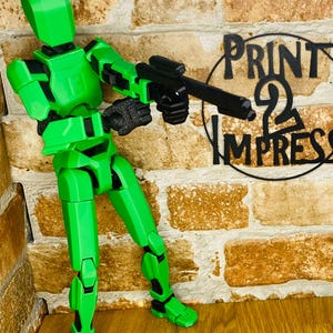 May include: A bright green articulated action figure holding a black rifle. The figure is posed against a brick wall with the words "PRINT 2 IMPRESS" in black lettering.
