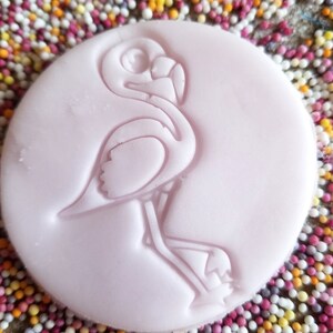 Peut inclure: Un tampon circulaire rose clair avec un motif de flamant rose. Le flamant rose est en relief sur le tampon, qui est entour&eacute; de vermicelles color&eacute;s. Le tampon est probablement utilis&eacute; pour la p&acirc;tisserie ou l'artisanat.