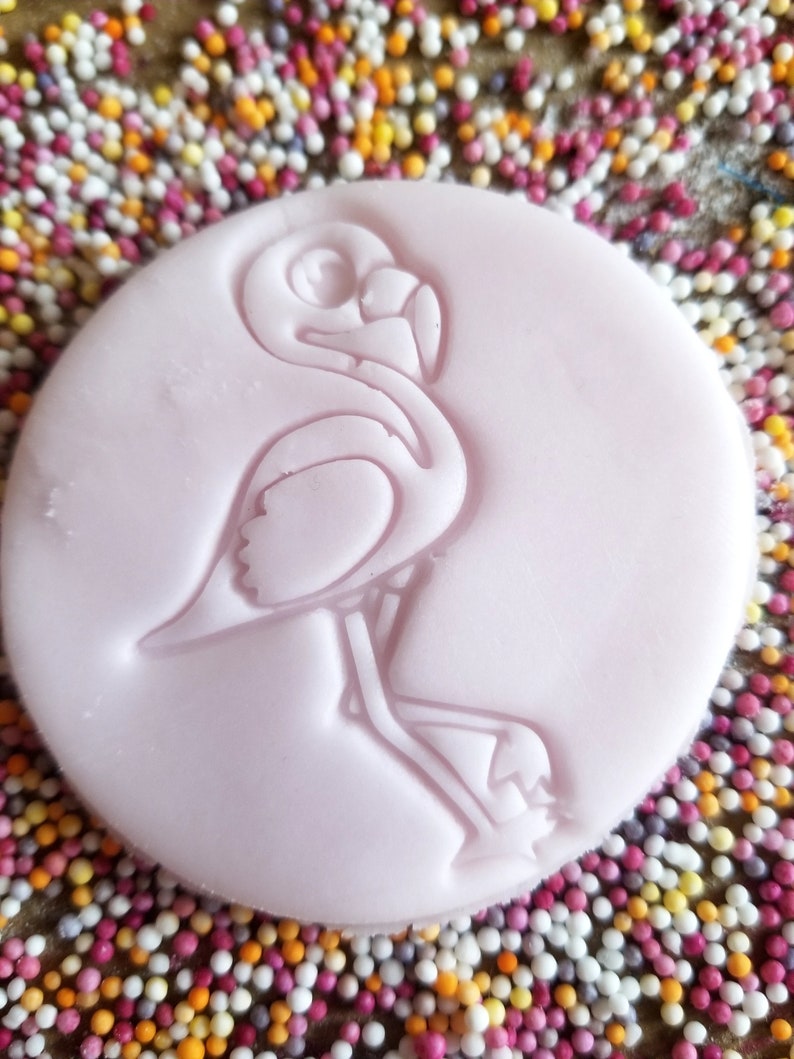 Peut inclure: Un tampon circulaire rose clair avec un motif de flamant rose. Le flamant rose est en relief sur le tampon, qui est entour&eacute; de vermicelles color&eacute;s. Le tampon est probablement utilis&eacute; pour la p&acirc;tisserie ou l'artisanat.
