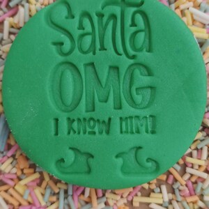 K&ouml;nnte beinhalten: Gr&uuml;ner runder Ausstecher mit dem Text "Santa OMG I know him!" und zwei Umrissen von Elfen-Schuhen.