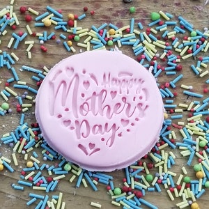 Puede incluir: Molde de silicona rosa con el texto "Happy Mother's Day" en una fuente cursiva. El molde est&aacute; rodeado de chispas de colores.
