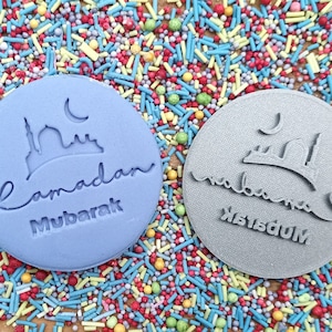 Pu&ograve; includere: Due timbri rotondi per biscotti con le parole "Ramadan Mubarak" e una silhouette di moschea. Uno &egrave; azzurro, l'altro grigio. I timbri sono circondati da zuccherini colorati.