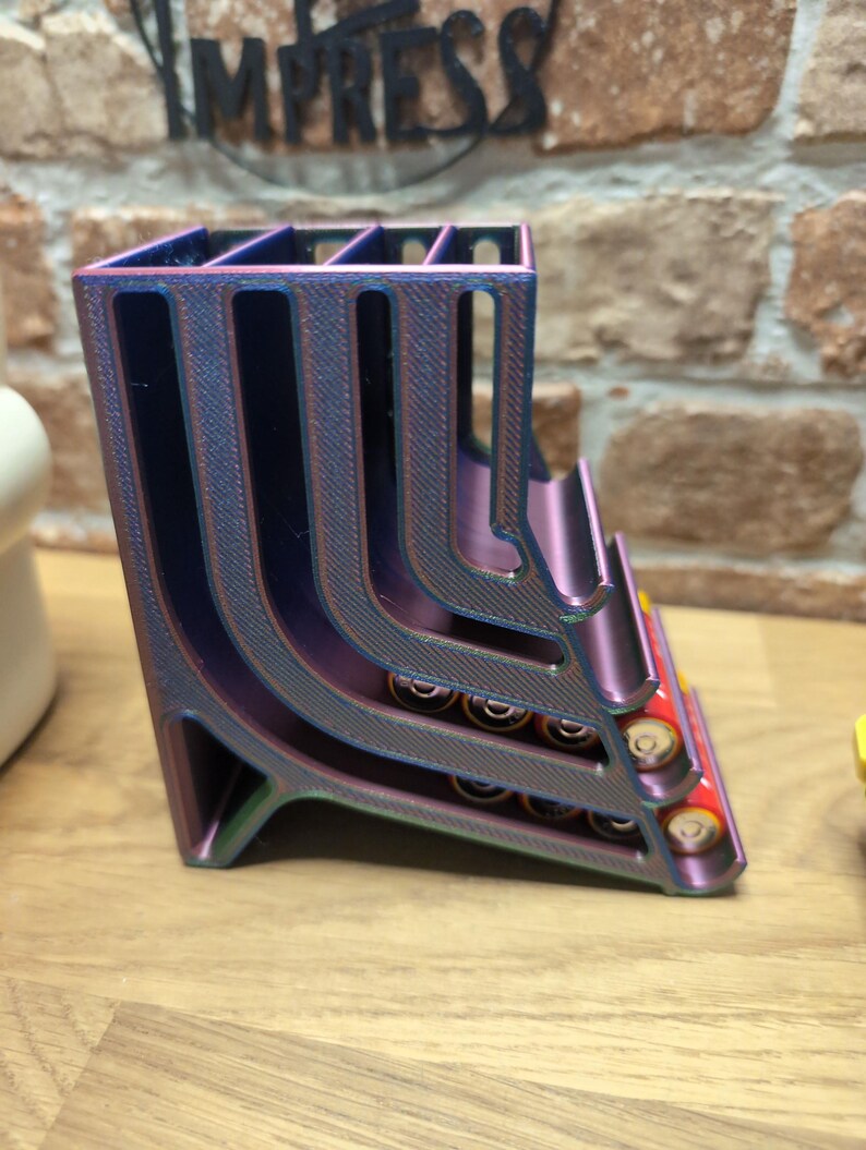 May include: A multi-colored, 3D-printed battery holder. The holder is a gradient of purple, blue, and green. It has multiple slots to hold batteries. The word "IMPRESS" is visible in the background.