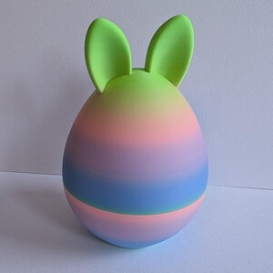 May include: A pastel pink, blue, and green ombre Easter egg with green bunny ears.