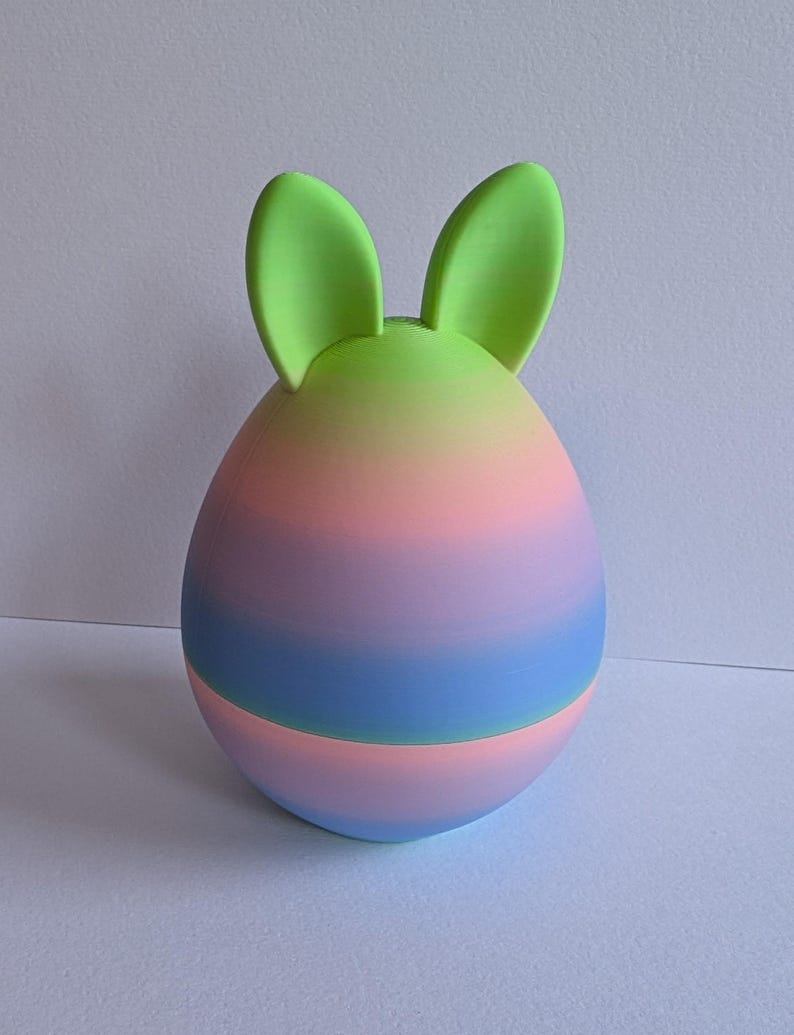 May include: A pastel pink, blue, and green ombre Easter egg with green bunny ears.