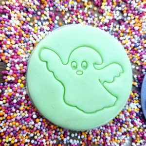 May include: A green cookie cutter shaped like a ghost with two eyes and a mouth. The cookie cutter is surrounded by colorful sprinkles.