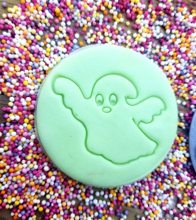 May include: A green cookie cutter shaped like a ghost with two eyes and a mouth. The cookie cutter is surrounded by colorful sprinkles.