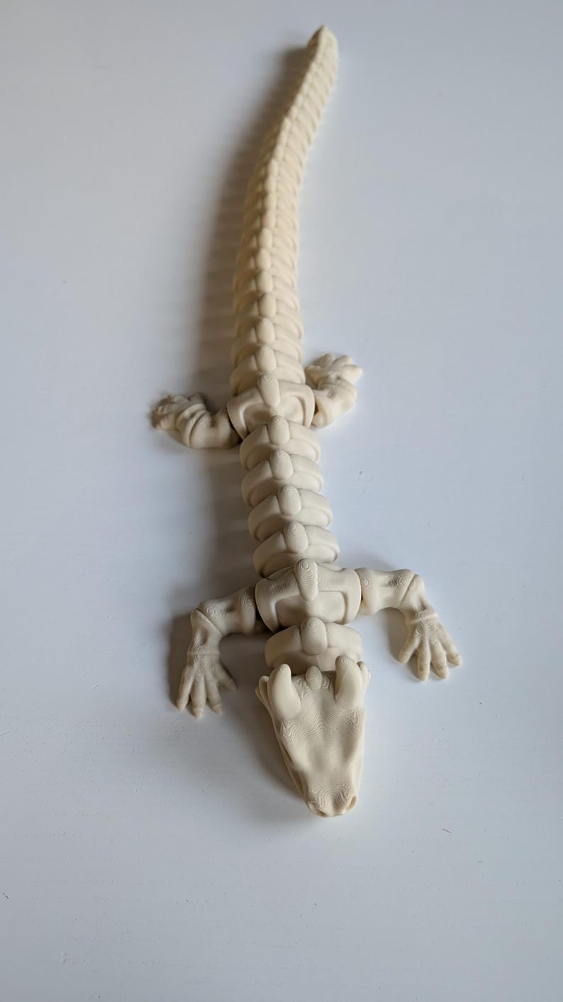 May include: A white articulated plastic toy lizard with a segmented body and a detailed head.