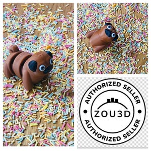 Op de afbeelding: Een bruine mopshond-figuur op een achtergrond van kleurrijke sprinkels. Het beeldje is gemaakt van flexibel materiaal en is in zittende positie geplaatst. De afbeelding bevat ook een zwarte en witte cirkel met de tekst "AUTHORIZED SELLER ZOU3D AUTHORIZED SELLER".