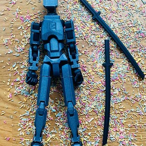 May include: A dark blue articulated action figure with a matching sword and a second sword piece. The figure is posed on a wooden surface covered in colorful sprinkles. The figure is approximately 6 inches tall.