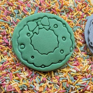 Peut inclure: Un biscuit vert avec un motif de couronne et un emporte-pi&egrave;ce gris avec le m&ecirc;me motif de couronne, le tout sur un lit de vermicelles color&eacute;s. La couronne a un n&oelig;ud en haut et de petits cercles autour.
