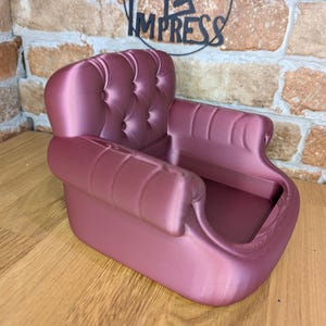 May include: A mauve-colored miniature sofa with a tufted back and rolled arms. The small decorative chair is made of a smooth material and has a classic design. The words "PRINT 2 IMPRESS" are in the background.