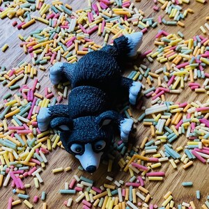 May include: A black and white dog figurine lying on its back on a surface covered in colorful sprinkles.