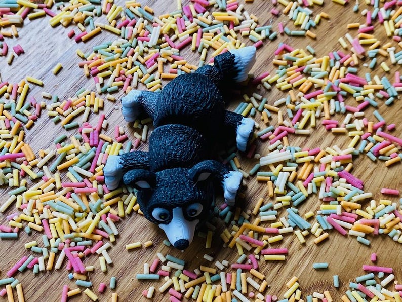 May include: A black and white dog figurine lying on its back on a surface covered in colorful sprinkles.