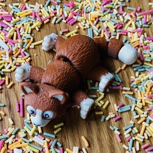 May include: A brown and white toy dog with a playful expression, lying on a wooden surface covered in colorful sprinkles.