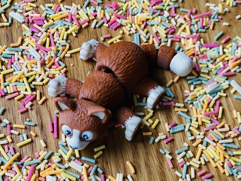 May include: A brown and white toy dog with a playful expression, lying on a wooden surface covered in colorful sprinkles.