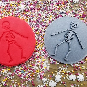 May include: Two round silicone molds for baking, one red and one gray, with a skeleton design.