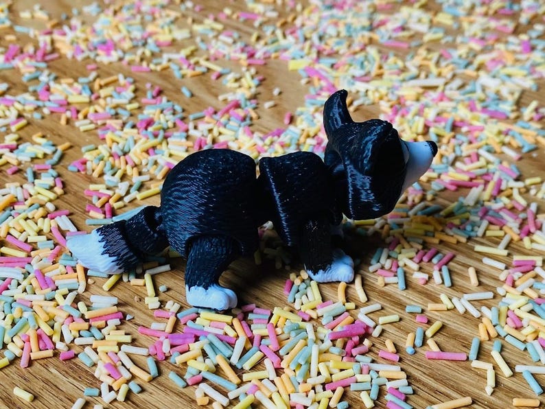 May include: A black and white toy dog figurine with a white tail and paws. The figurine is standing on a surface covered in colorful sprinkles.