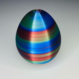 May include: A colorful, striped, egg-shaped object with a smooth, glossy finish. The egg is decorated with alternating bands of red, blue, green, and light blue.