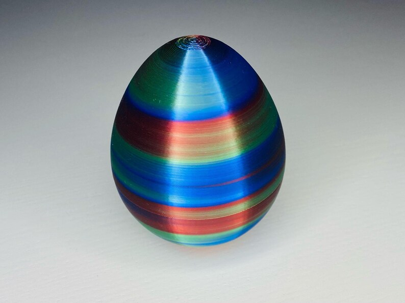 May include: A colorful, striped, egg-shaped object with a smooth, glossy finish. The egg is decorated with alternating bands of red, blue, green, and light blue.