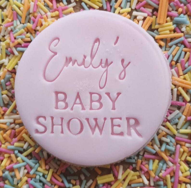 Op de afbeelding: Een ronde roze koek met de tekst "Emily's Baby Shower" in roze letters.