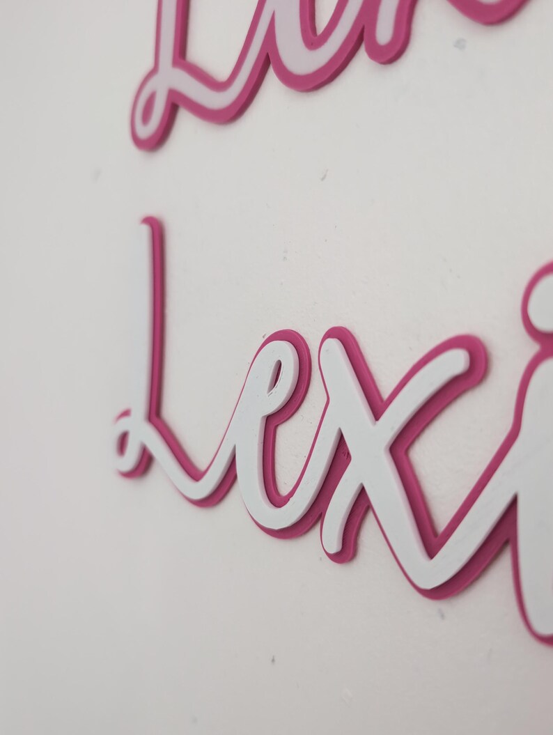 May include: A white and pink layered name sign with the name "Lexi" in cursive script.