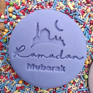 Pu&ograve; includere: Un biscotto rotondo, viola chiaro, con la scritta &laquo;Ramadan Mubarak&raquo; e un disegno di moschea e luna crescente. Circondato da zuccherini colorati.