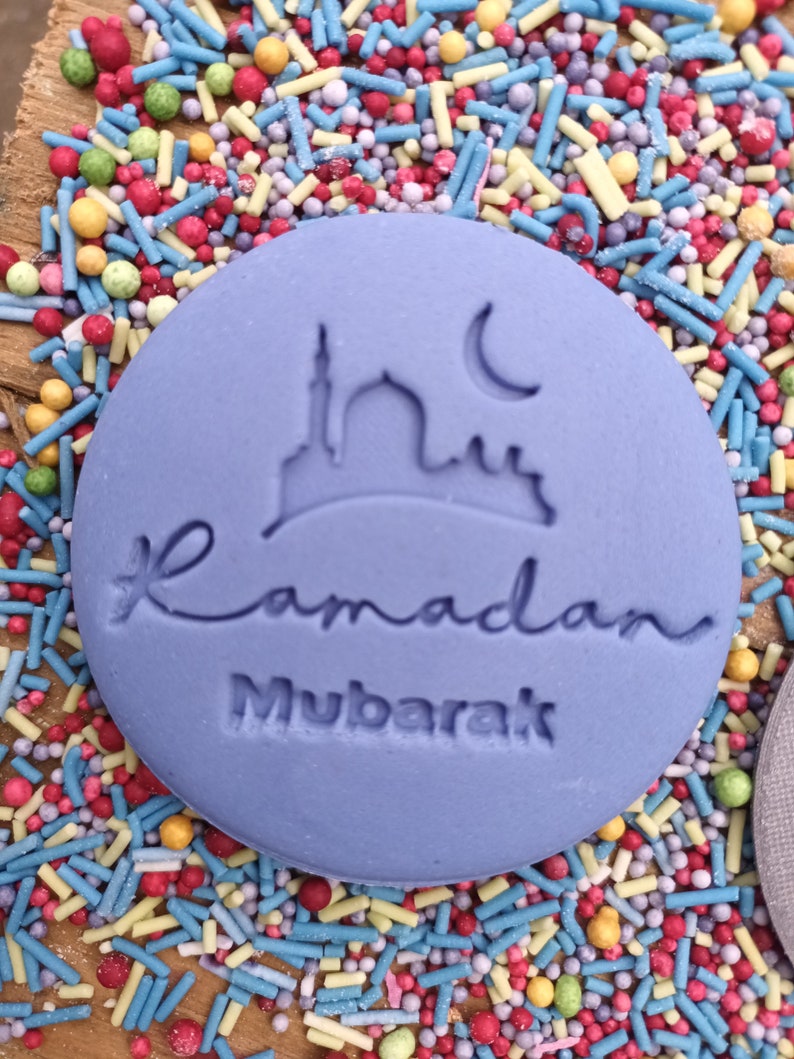 Pu&ograve; includere: Un biscotto rotondo, viola chiaro, con la scritta &laquo;Ramadan Mubarak&raquo; e un disegno di moschea e luna crescente. Circondato da zuccherini colorati.